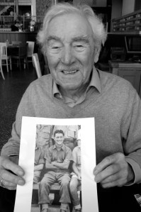 Bill Rae, 94, holding a 1941 photo of himself as a Prisoner of War in Italy.