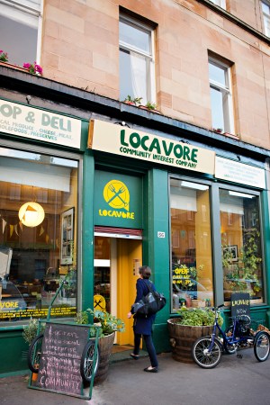 The green and yellow shopfront of the Locavore Community Interest Company, with a person walking through the front door