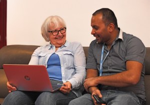 A man and an older women sitting together on a couch and working on a laptop