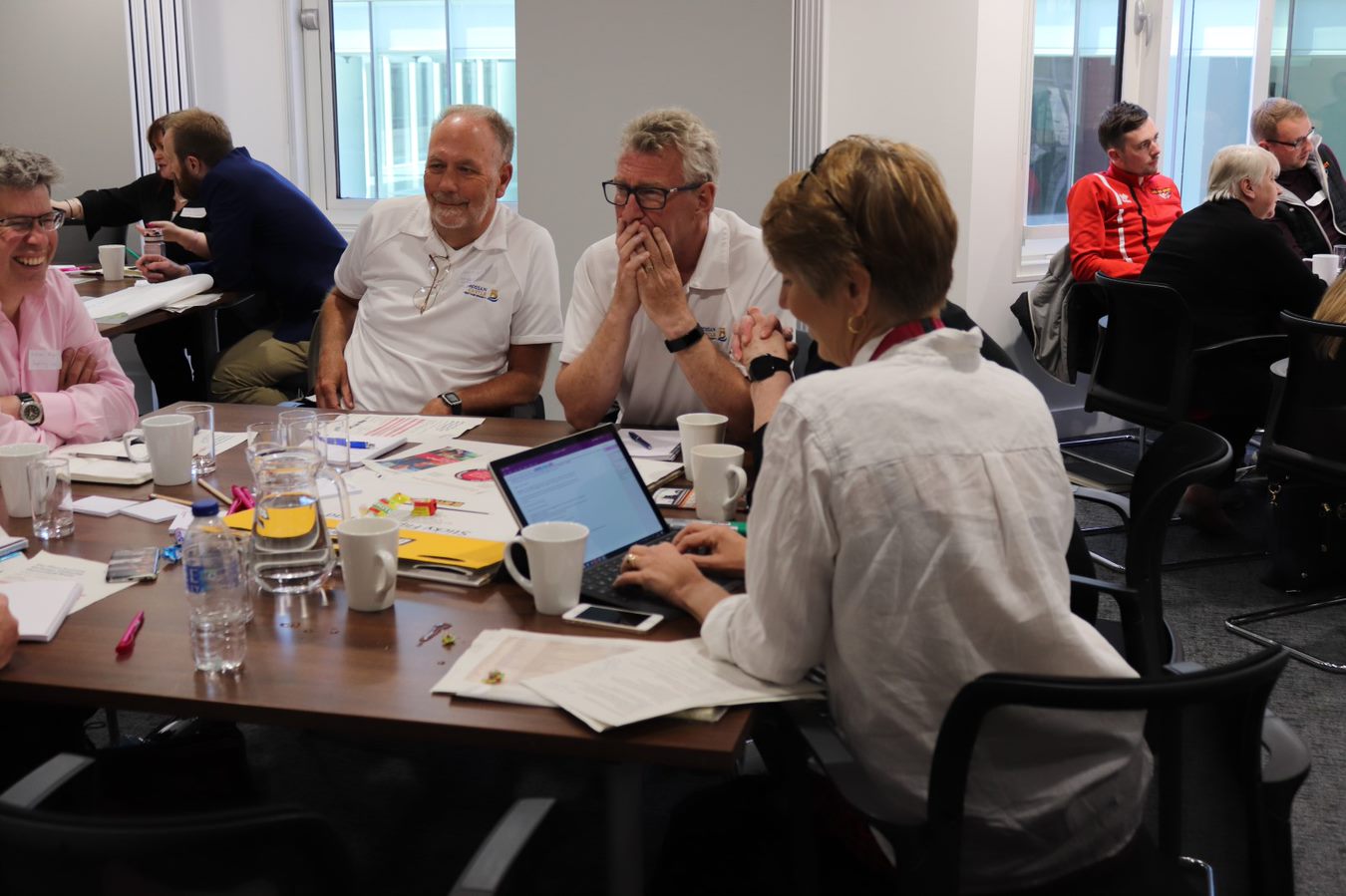 Alison typing on her laptop in front of a group of people laughing