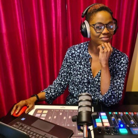 Jambo! radio presenter Bene Briggs-Mckinley wearing headphones and sat behind her laptop, microphone and mixing desk at her home studio.
