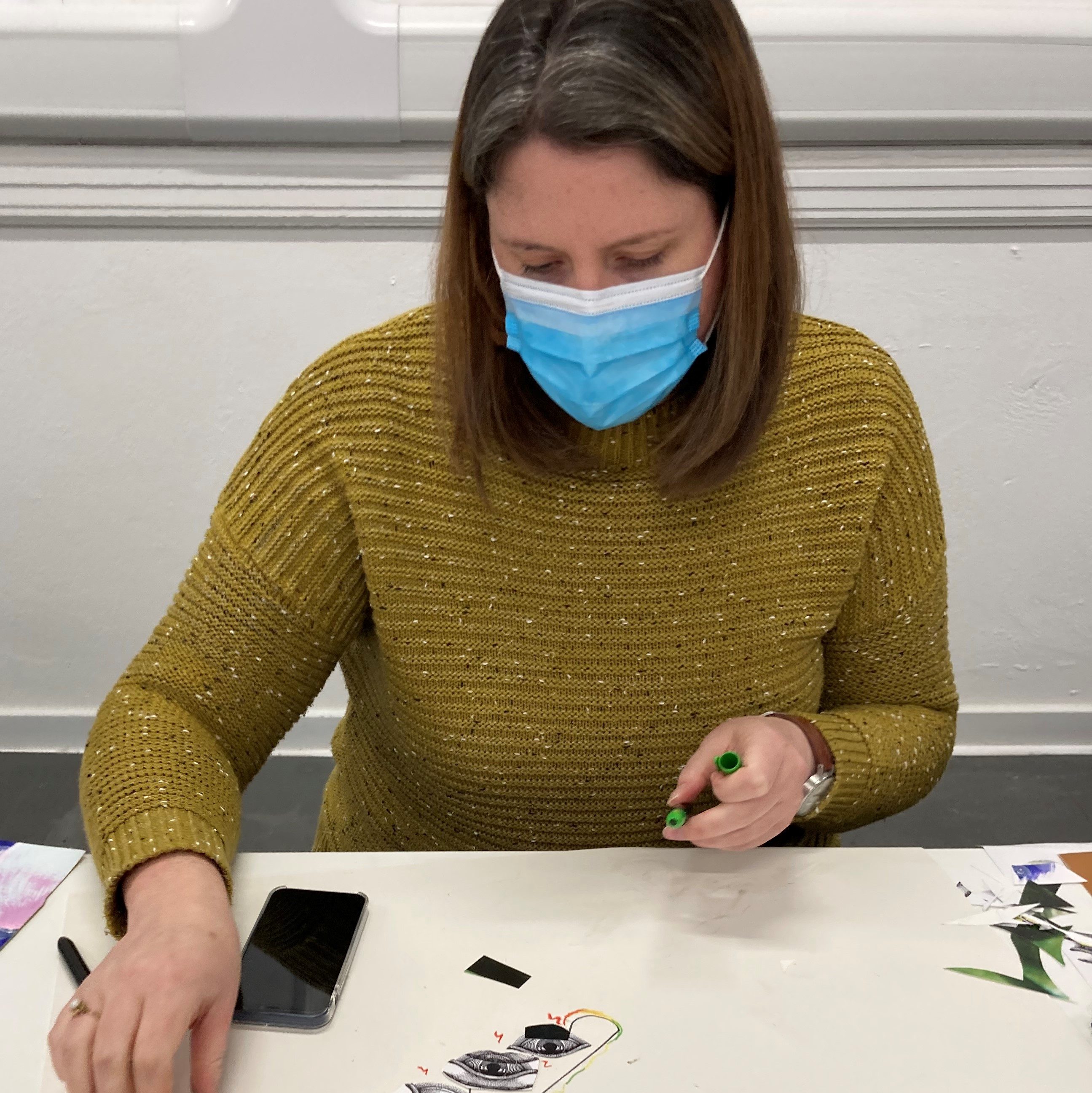 The person holds a pen in one hand as they draw on a large piece of paper. They have drawn three eyes so far but the work is not finished.