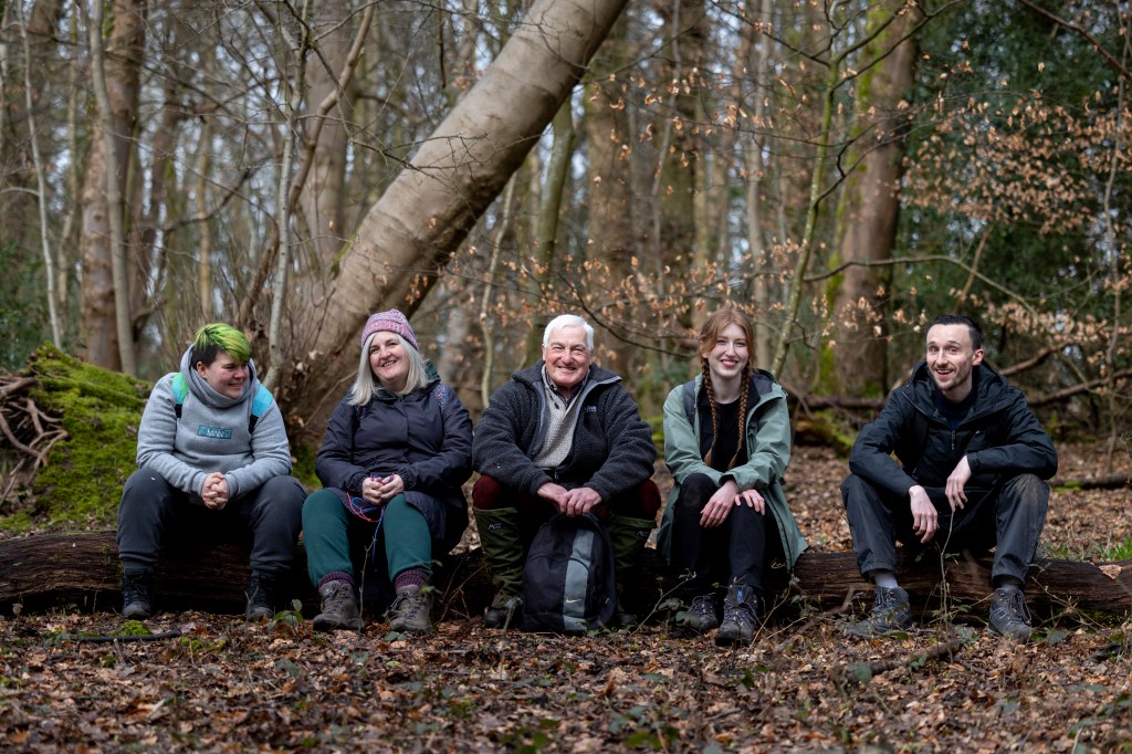 Inchinnan Development Trust. A woodland project which supports people in the community get together and get in touch with the outdoors to improve their wellbeing. The group sit on a log.