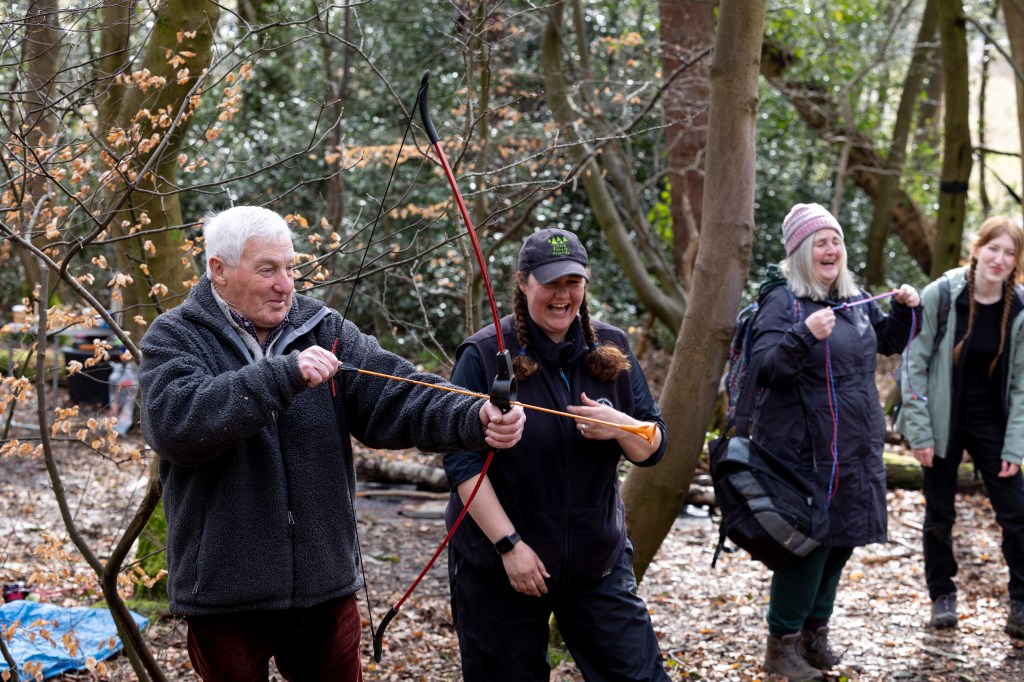 a group of people in a woodland area, they are practicing archery.
