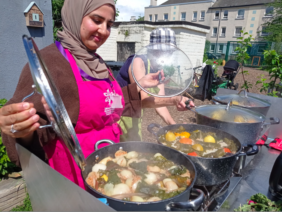 Two people cook outside. There are 4 large pots filled with delicious food ready to be served to members of the community group.
