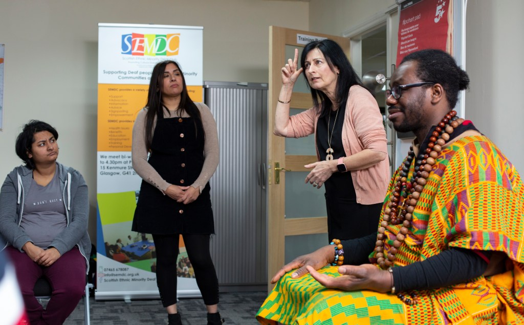 4 people engage in an information session. They are using sign language.